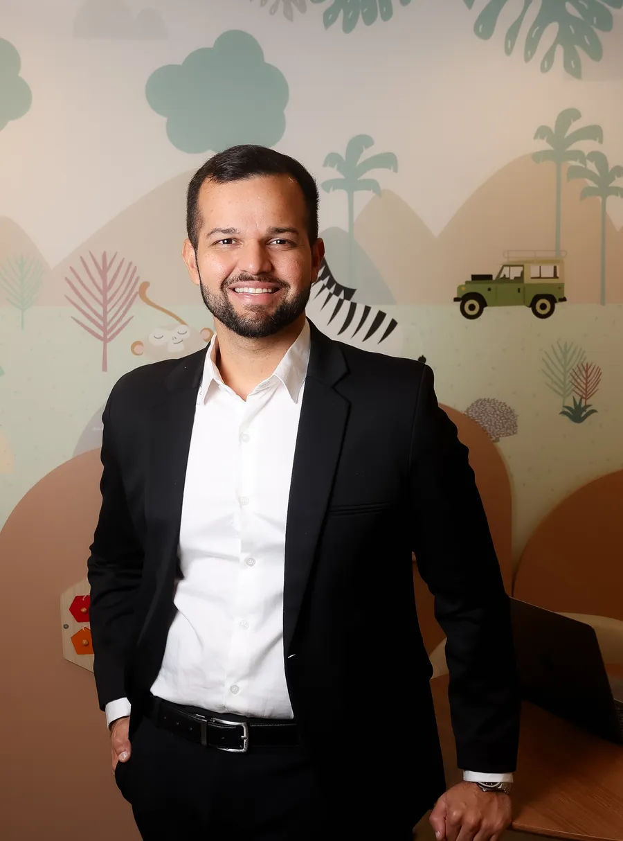 Dr. Bruno William, alergista pediátrico, sorrindo em consultório infantil